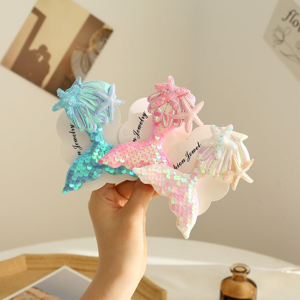 Colorful mermaid tail barrettes displayed on a table, featuring starfish designs and shimmering sequins for girls' hair.