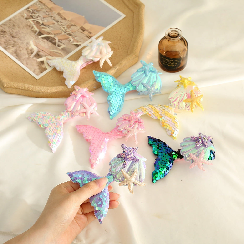 Colorful mermaid tail barrettes displayed on a table, featuring starfish designs and shimmering sequins for girls' hair.